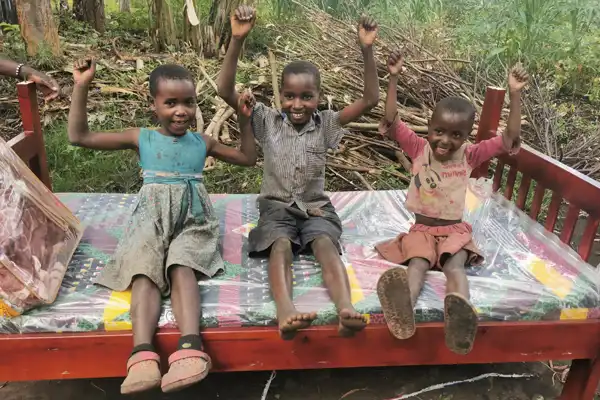 3 Niñas de Uganda con expresión feliz sobre una cama en el campo